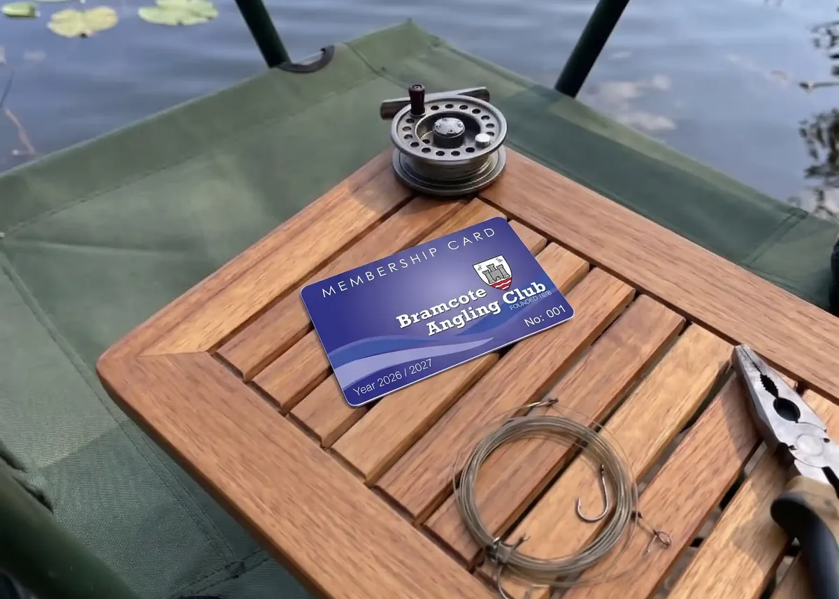 Bramcote Angling Club membership card on a wooden tackle table by the lake