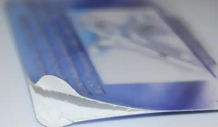 the corner of a cheap plastic card peeling apart to show the white paper core inside it