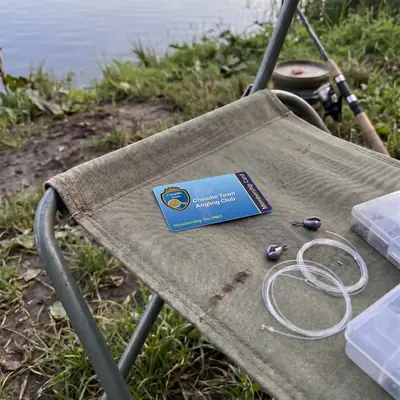 Blue angling club membership card on a bankside chair with fishing line