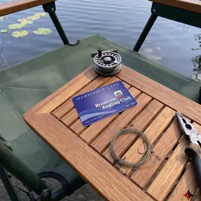 Bramcote Angling Club membership card on a wooden tackle table by the lake
