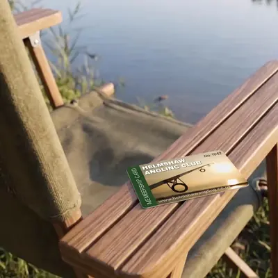 Helmshaw Angling Club numbered membership card on a lakeside chair