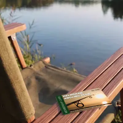 Helmshaw Angling Club numbered membership card on a lakeside chair