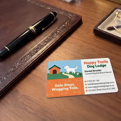 Happy Trails Dog Lodge plastic business card on a leather desk
